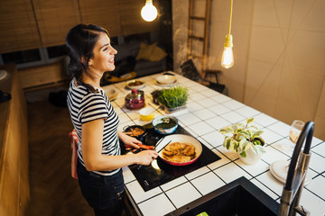 Young woman tasting a healthy meal in home kitchen.Making dinner on kitchen island standing by...
