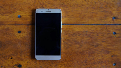 A bar shape smartphone on wood table and have some space for write wording, necessary device for new generation lifestyle and work life that support convenient working anywhere and sharing anytime