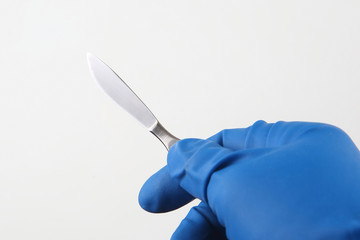 Medical scalpel in hand wearing blue gloves - obrazy, fototapety, plakaty