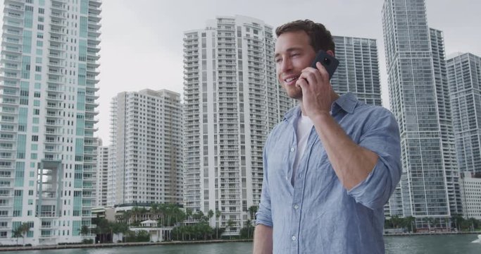 Young Businessman Portrait Using Phone Walking In Miami. Smiling Confident Business Man Walking Using Cell Smartphone Front Of Modern Condo Building. City Lifestyle People In Miami, Florida, USA.