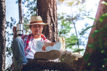 hiker sitting and look at map with cup in the forest on old wood.