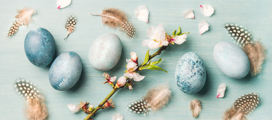 Painted traditional eggs for Easter holiday, feathers and blooming almond flowers on branch over...