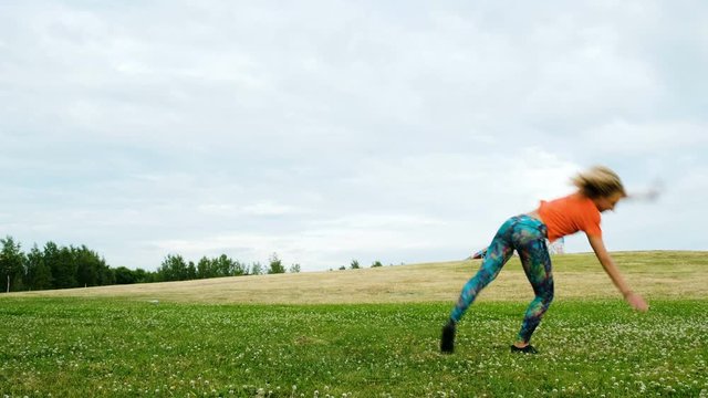Woman makes a wheel and coups on her hands in nature, girl gymnast trains in a city park
