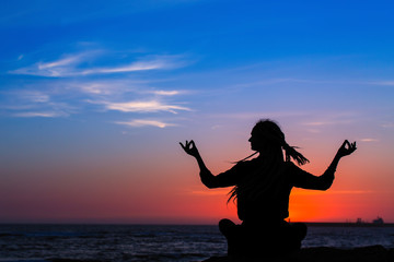 Fototapeta premium Yoga woman meditation silhouette. Healthy lifestyle on the ocean during amazing sunset.