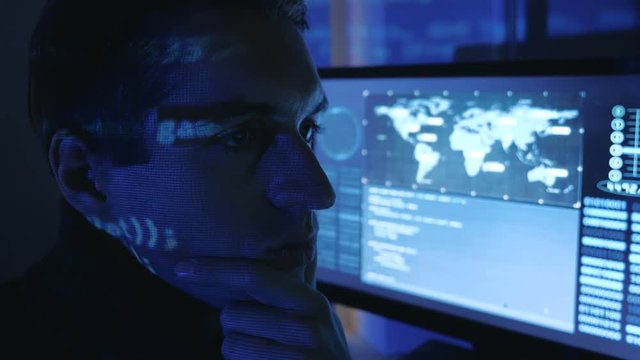 Close-up portrait of a Man Professional Developer Programmer in a data center filled with monitor screens. Hacker works at a computer at night in a dark office.