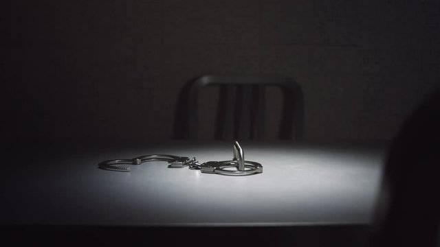 Medium tracking shot of a pair of handcuffs on a table in an interrogation room.