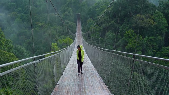 Young woman walking on the Situ Gunung Suspension Bridge while enjoying the forest landscape in Sukabumi, West Java, Indonesia. Shot in 4k resolution