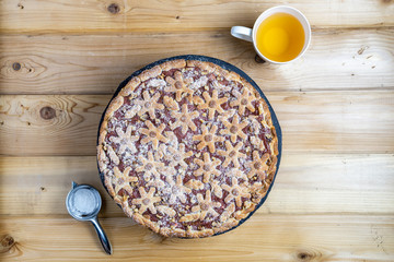 cake with berries and rhubarb and cup of tea on a wooden table.