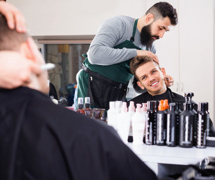 Male hairdresser accurately cutting beard