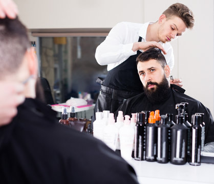 concentrated male stylist creating haircut for man client at hairdressing salon