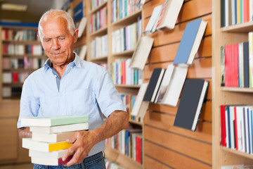 Portrait of intelligent older man in library with pile of books in hands
