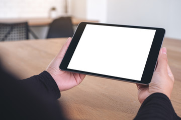 Mockup image of hands holding and looking at black tablet pc with blank white screen while sitting in office