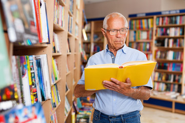 Focused elderly man looking for information in books in bookstore