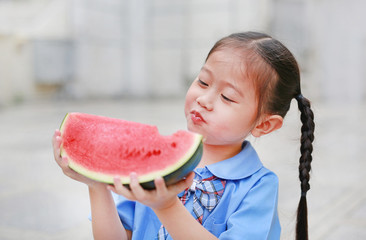 Adorable little Asian child girl in school uniform enjoy eating watermelon.