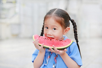 Cute little Asian child girl in school uniform enjoy eating fresh sliced watermelon.