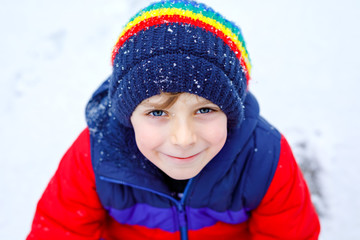 Portrait of little school kid boy in colorful clothes playing outdoors during snowfall. Active leisure with children in winter on cold snowy days. Happy healthy child having fun and playing with snow.