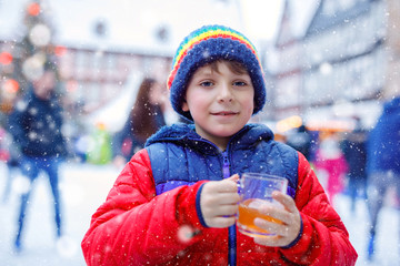 Happy little kid boy in colorful warm clothes on skating rink of Christmas market or fair drinking hot punch or chocolate. Healthy child having fun on ice skate. people having active winter leisure