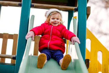 Cute toddler girl having fun on playground. Happy healthy little child climbing, swinging and...