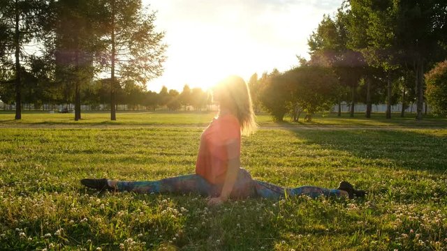 Gymnast woman sits on the longitudinal and transverse splits. Stretching in the city park