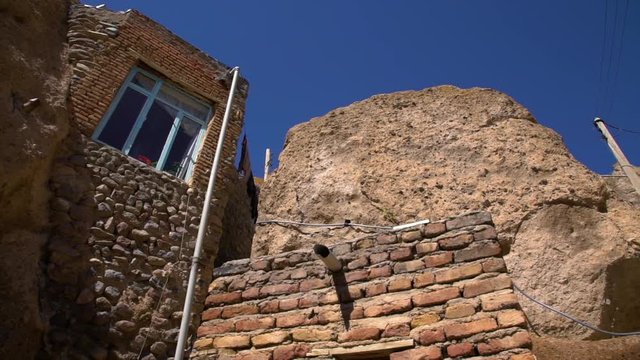Handheld, low angle, wide, exterior, panning shot of clothes drying and window built into the rocks at the Kandovan Village.
