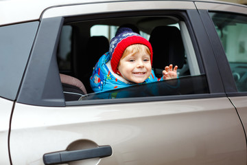 Portrait of pretty toddler boy sitting in car seat. Child transportation safety. Cute healthy kid boy looking happy about family vacations with car through window during standing in traffic jam