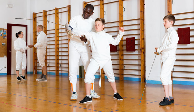 Focused boys fencers attentively listening to professional fencing coach in gym