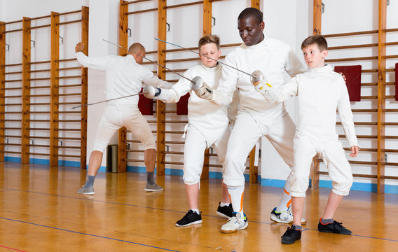 Focused boys fencers attentively listening to professional fencing coach in gym