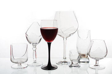 A glass of red wine on the background of broken glasses on a light background