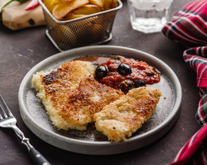 Fried fish with tomato-olive sauce and potatoes.