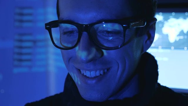 Close-up portrait of a Man Professional IT Programmer in a data center filled with monitor screens. Hacker works at a computer at night in a dark office.