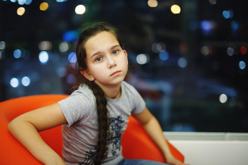 Teenager girl with a long braid in an orange chair.