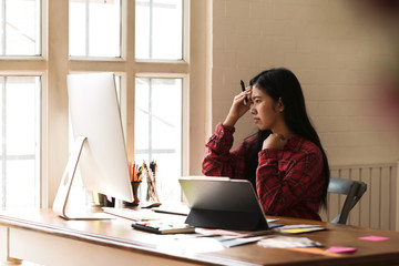 Frustrated Asian graphic designer thinking solving problem working on desktop computer in studio.