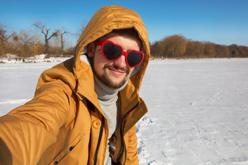 Breaded man doing selfie on winter sunny day. Heart sunglasses.