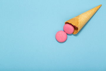 Waffle cone with colorful macaron or macaroon on blue pastel background top view. Flat lay composition.