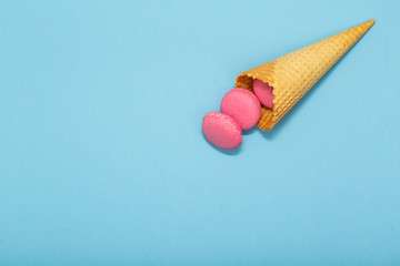 Waffle cone with colorful macaron or macaroon on blue pastel background top view. Flat lay composition.