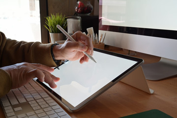 Cropped shot of designer using graphics tablet while working with computer at studio or office