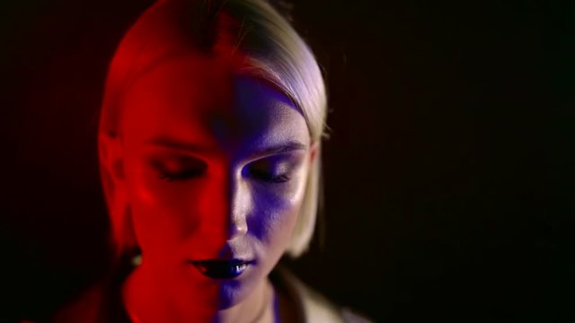 blonde woman with bright fashion make-up is posing for camera in darkness, red and blue spotlights