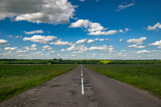 Asphalt road through the green field and clouds on blue sky in summer day