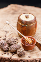 Barrel with honey and honey stick on a wooden background with pine nuts and pine cones. Textured wood products.