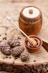 Barrel with honey and honey stick on a wooden sawn and pine nuts and cones. Textured wood products.