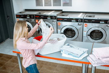 Young woman sorting clothes for washing standing in the self service laundry