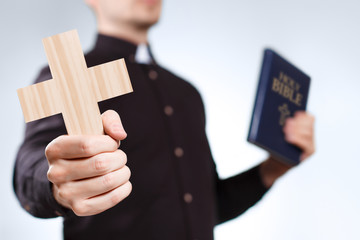 Priest holding a cross and the Holy Bible on grey background