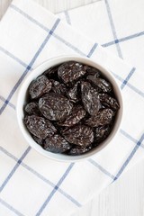 Full bowl of dry prunes on a white wooden background, overhead view. Flat lay, from above, top view.