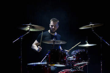Fototapeta na wymiar music, people, musical instruments and entertainment concept - male musician with drumsticks playing drums and cymbals at concert or studio