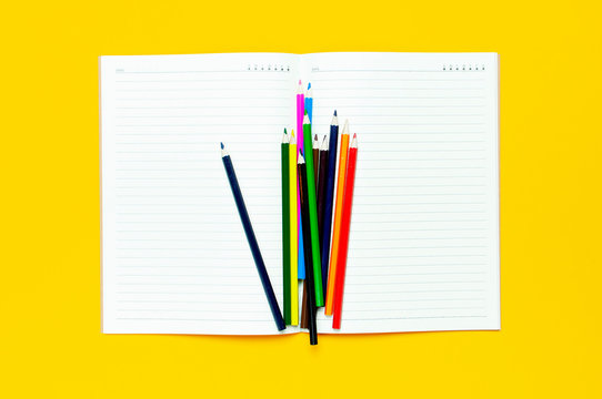 Color pencils and clean notebook in line on yellow background top view flat lay copy space. Wooden colored pencils for drawing, objects for creativity, school supplies close-up. Back to school concept