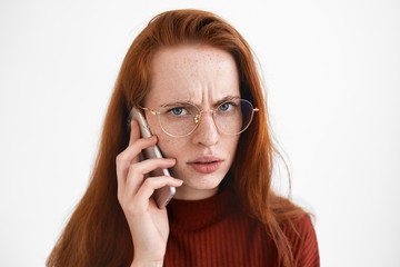 Picture of displeased ginger girl in stylish eyewear frowning while making phone calls to taxi service, being dissatisfied while waiting for cab too long. Negative human expressions and technology