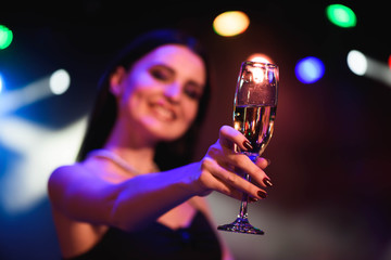 Young celebrating woman black dress, holding a glass of champagne. Party.