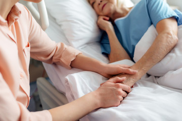 cropped view of daughter sitting near senior mother in bed and holding hands in hospital