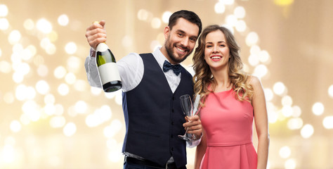 celebration and people concept - happy couple with bottle of champagne and glasses over festive lights background