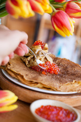 Pancakes for the traditional Russian spring holiday. Thin pancakes with red caviar and a bouquet of fresh tulips. Wooden background and festive food.